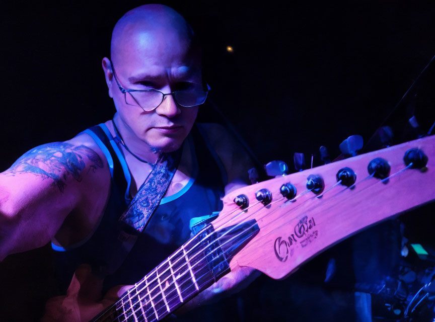 Tattooed guitarist playing electric guitar on dark stage