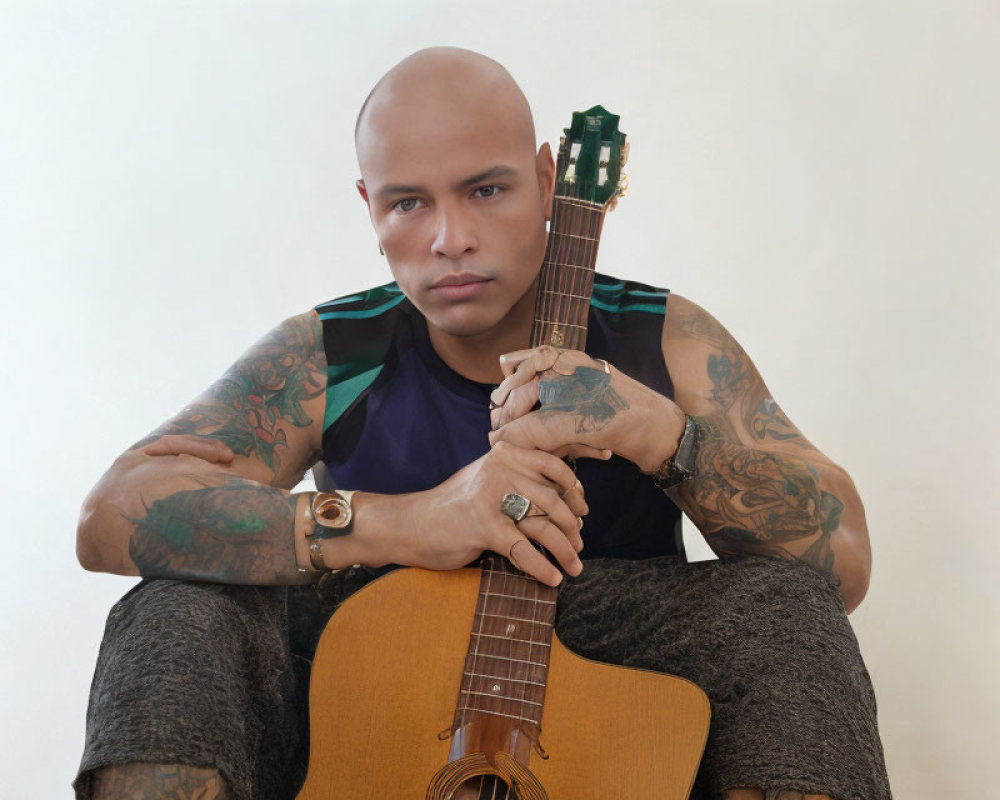 Bald person with arm tattoos holding acoustic guitar in sleeveless top