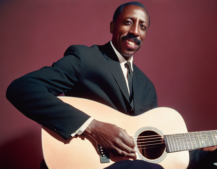 Man in Black Suit Smiling Playing Acoustic Guitar on Red Background