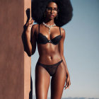 Woman with large afro in lace lingerie and sunglasses against terracotta wall with chunky necklace.