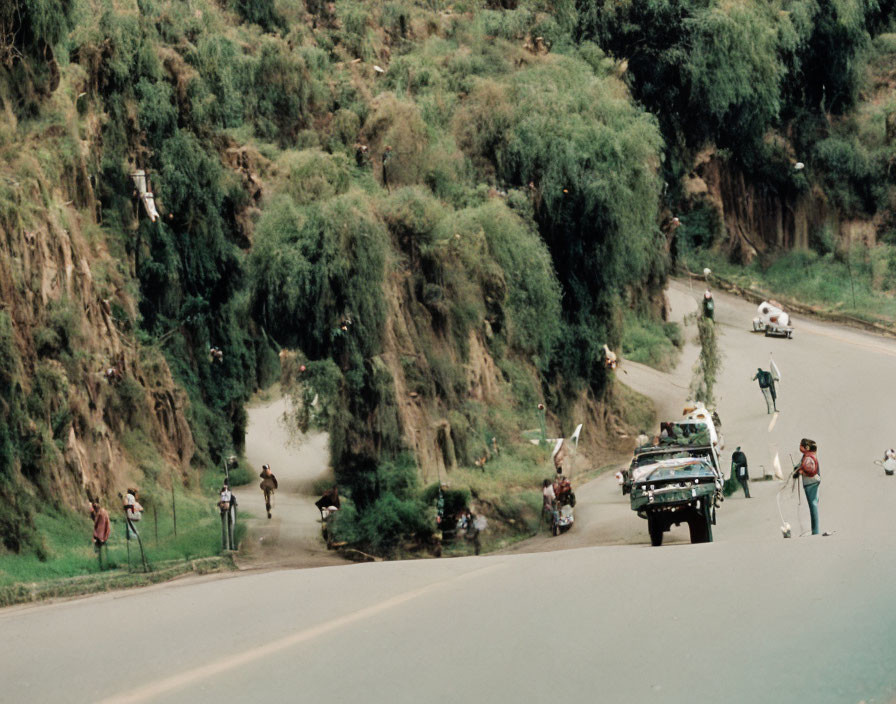 Road race scene with spectators, participants, support vehicle, and green hillside.