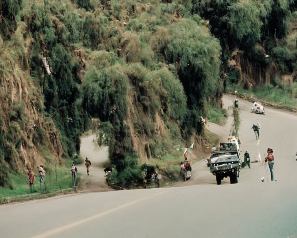 Road race scene with spectators, participants, support vehicle, and green hillside.