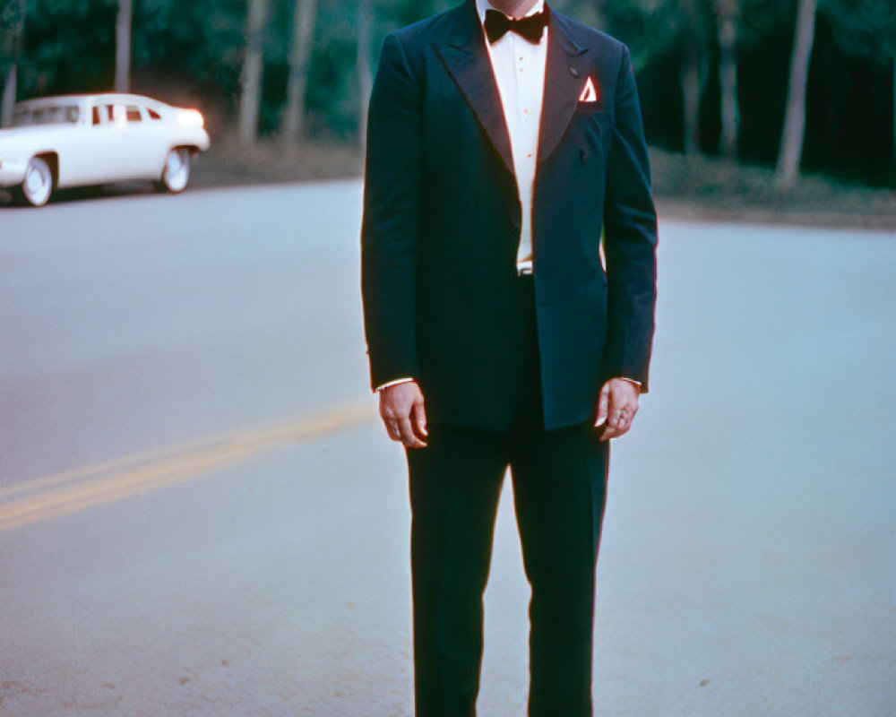 Man in Black Tuxedo with Red Pin Standing by Vintage Car and Trees