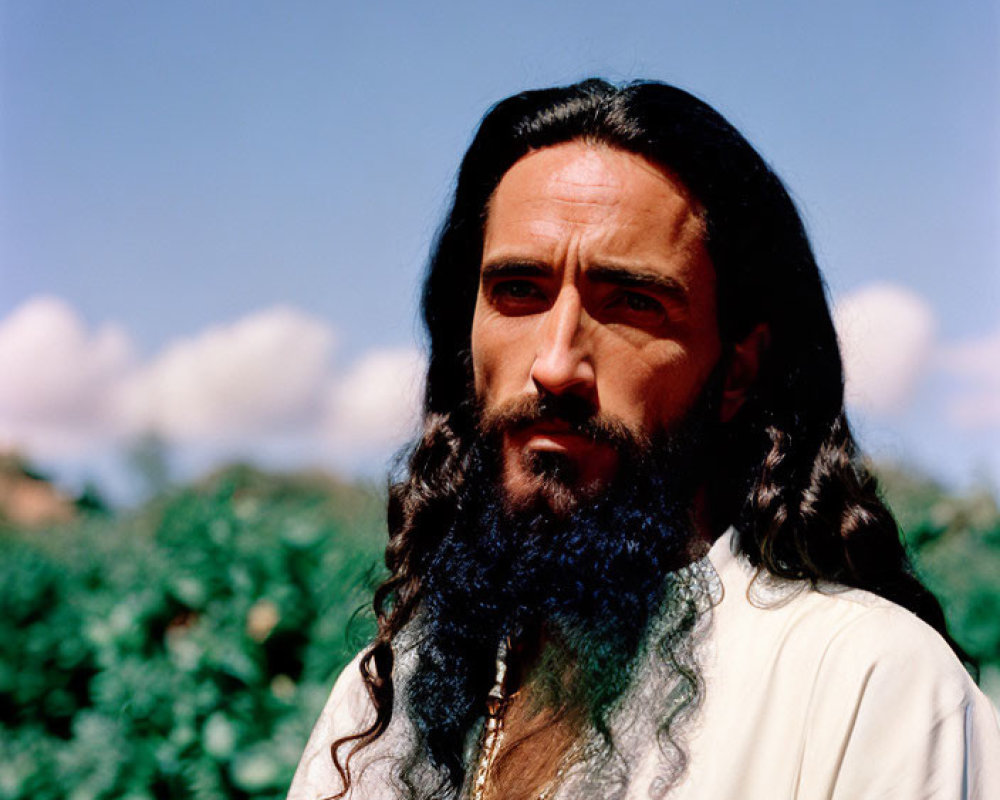 Bearded man in white robe and gold necklace outdoors