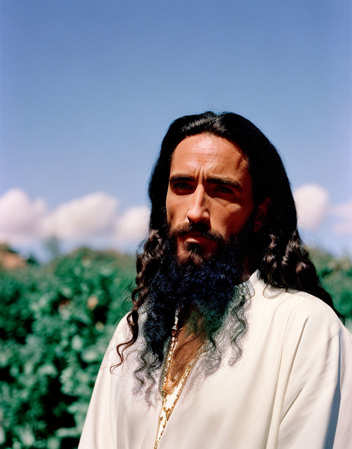 Bearded man in white robe and gold necklace outdoors