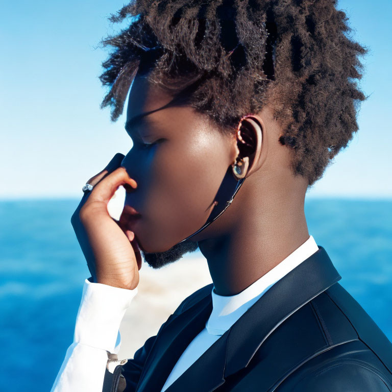 Stylish person with afro in suit by sea, touching sunglasses