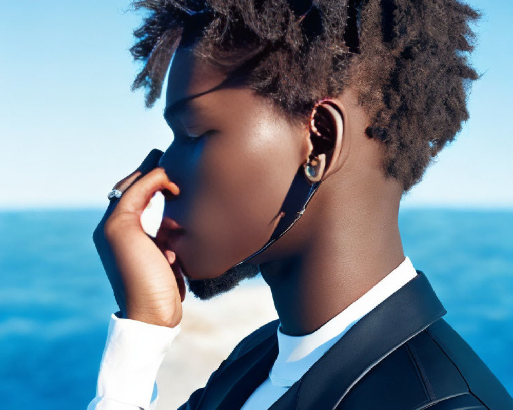 Stylish person with afro in suit by sea, touching sunglasses