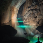 Silhouetted figures on rocks near towering monolith in glowing mist