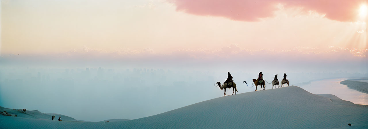 Desert sunrise with silhouetted figures on camels and distant city haze.