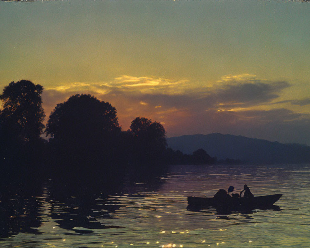 Silhouette of person rowing boat on calm river at sunset