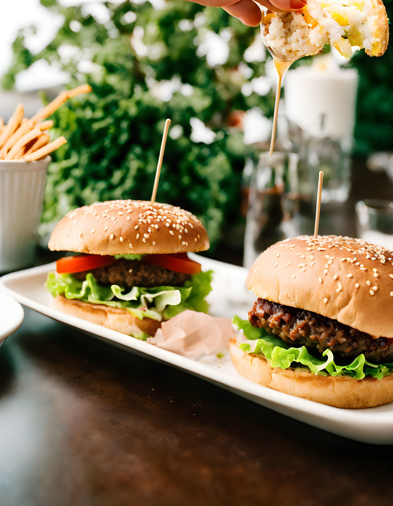 Juicy burgers with lettuce and tomato, fries dipped in sauce, blurred salad on plate