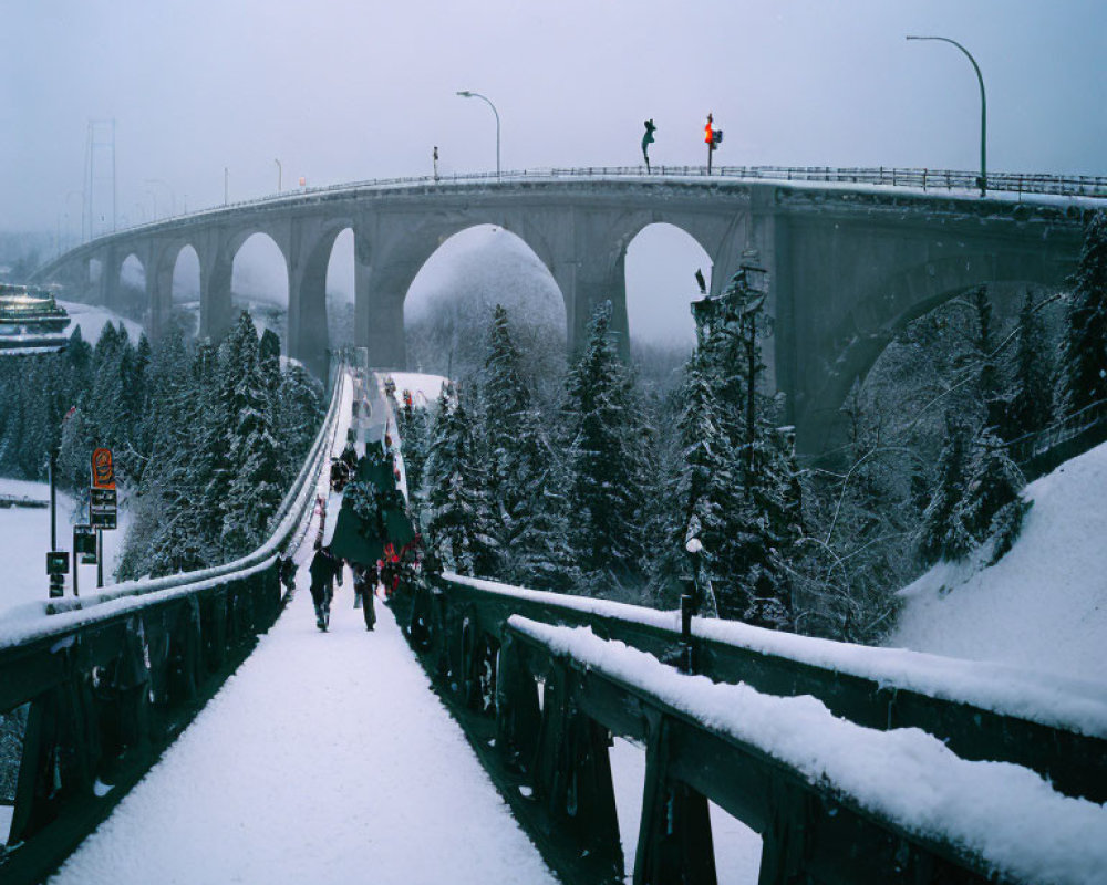 Snow-covered bridge with pedestrians, trees, arch, and traffic light under hazy sky