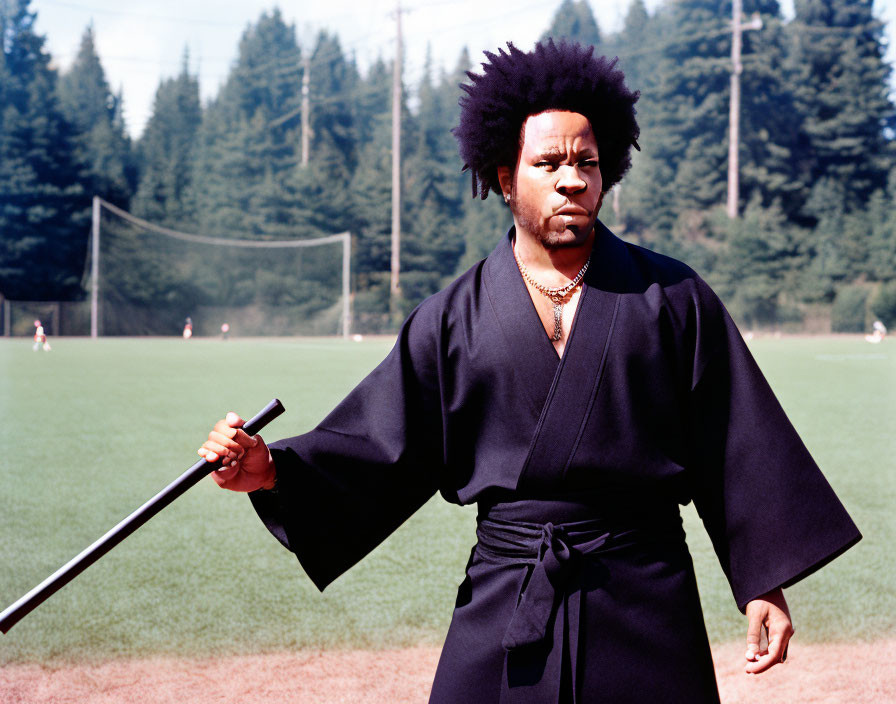 Person with Afro Hairstyle in Martial Arts Attire with Sword Outdoors