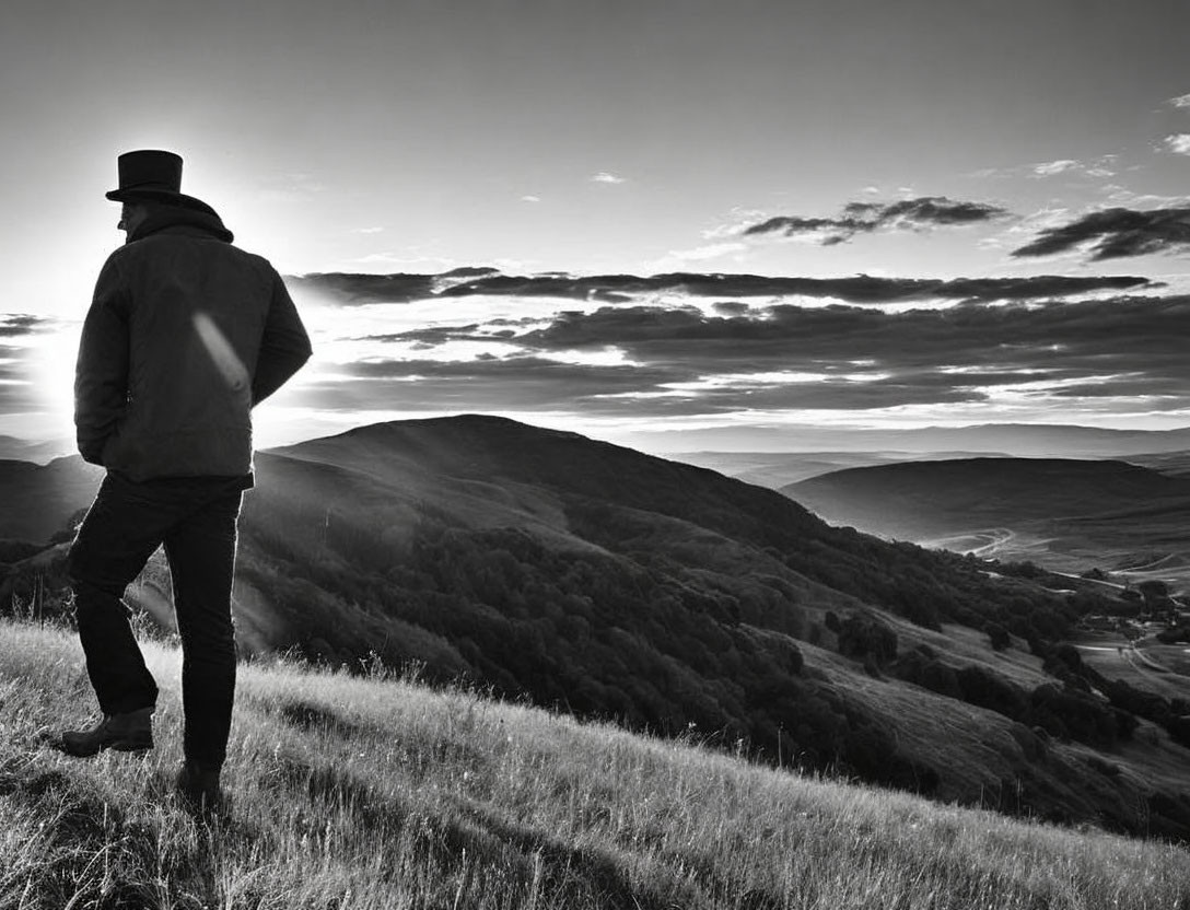 Person in Hat and Jacket on Grassy Hill with Rolling Hills in Background