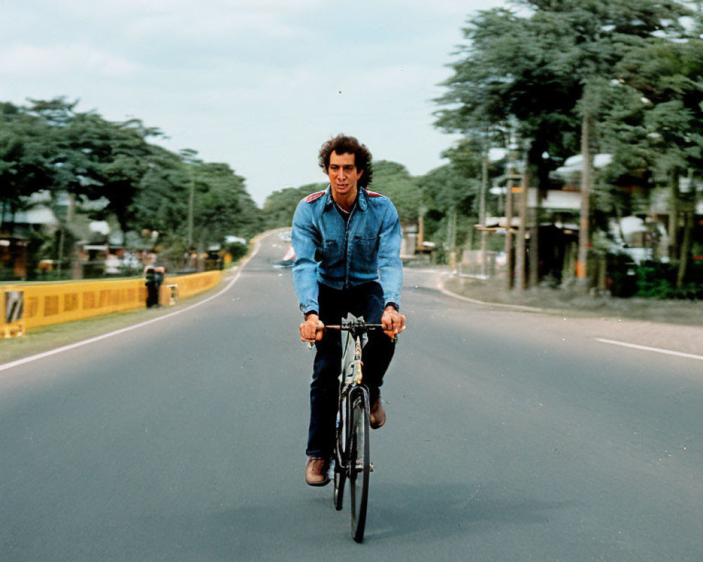 Man in Blue Jacket Riding Bicycle on Empty Road with Trees and Cloudy Sky