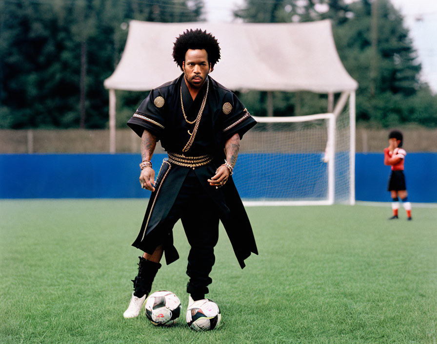 Man with Afro Hairstyle in Ornate Clothes on Soccer Field with Balls and Goal