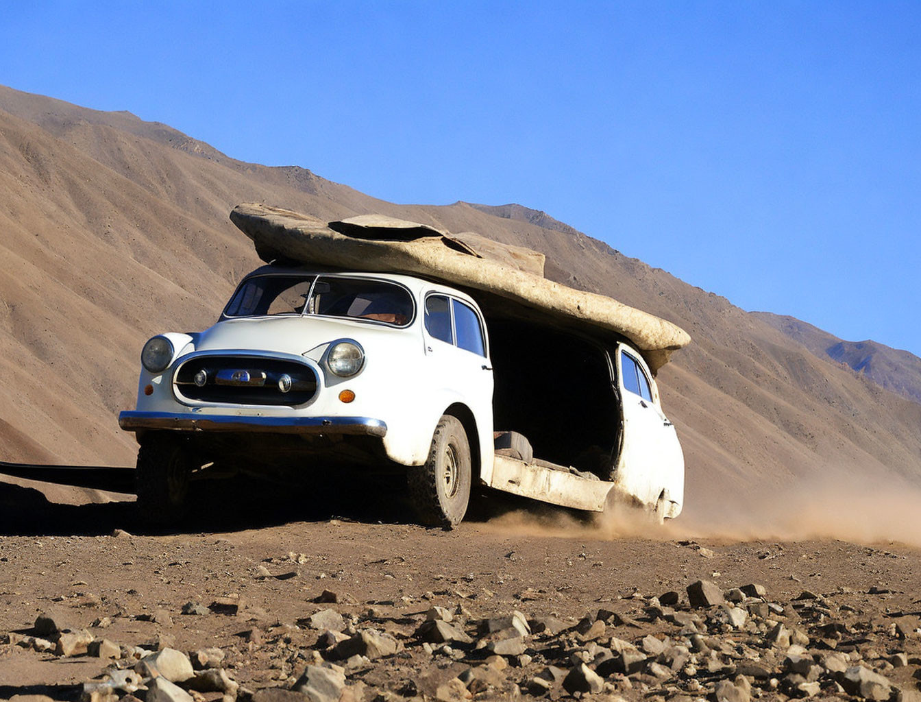 Vintage white car with surfboard on dusty terrain under blue skies and barren hills