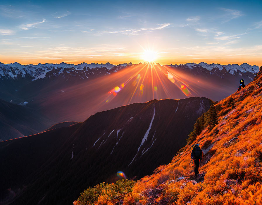 Mountain trail hikers admire sunset over orange foliage and peaks with sunrays.