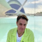 Man in lime green jacket with slicked-back hair against cloudy sky