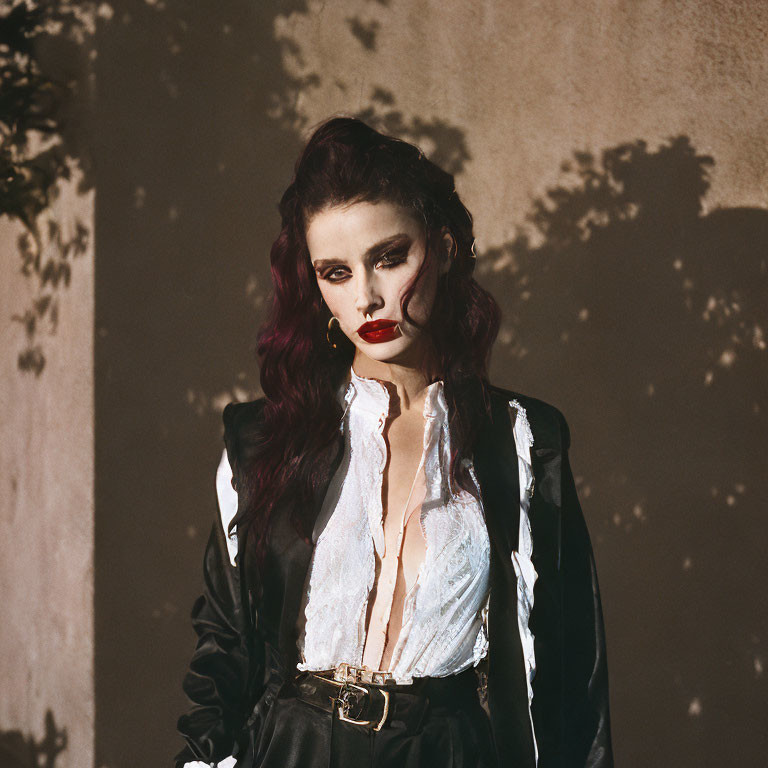 Woman in dark makeup and red lipstick standing against shadow-patterned wall