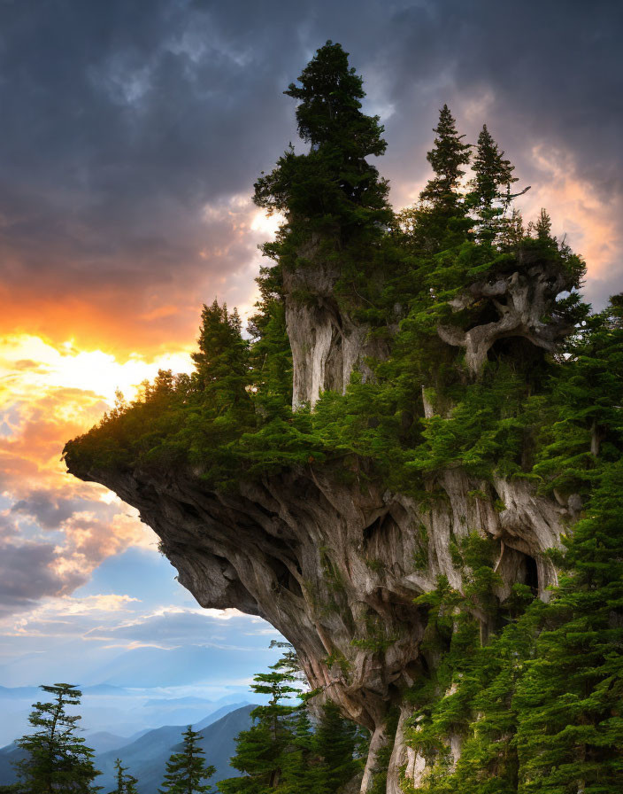 Scenic sunset view of cliff, trees, and mountains with sunbeams.