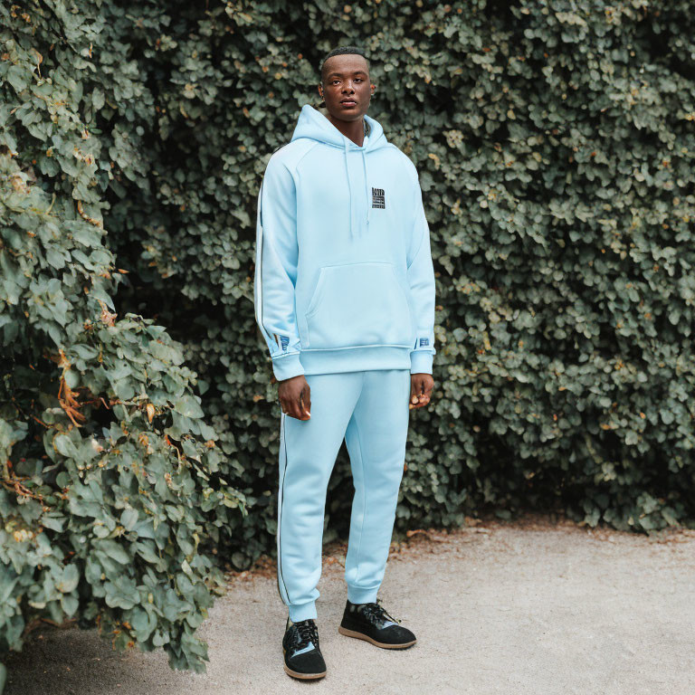 Man in Light Blue Hoodie and Matching Pants on Green Leafy Background