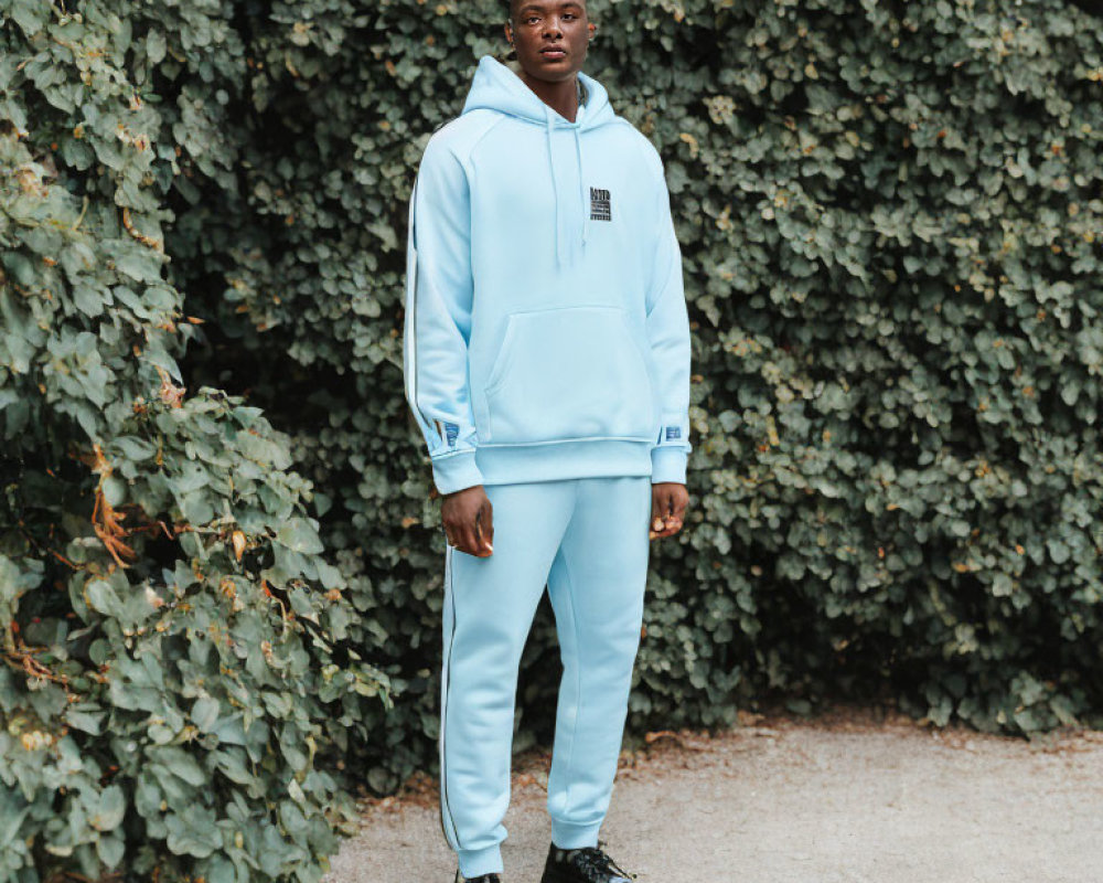 Man in Light Blue Hoodie and Matching Pants on Green Leafy Background