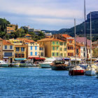 Vibrant seaside town painting with sailboat, patterned buildings, and rolling hills