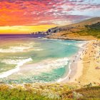 Colorful painting of rolling waves, vibrant sky, and coastal town