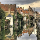 Medieval village with stone houses, red roofs, bridge, calm river, lush landscape