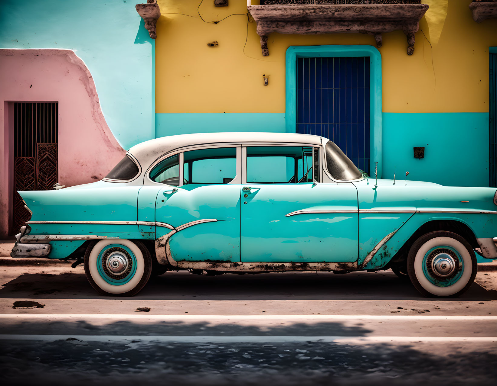 Vintage turquoise car with white wall tires in front of colorful buildings on a sunny day