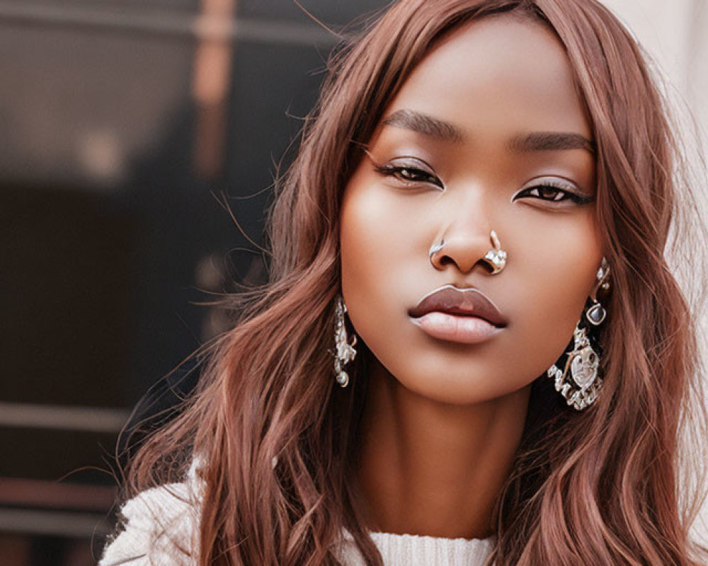 Woman with septum piercing and earrings in white sweater, gazing at camera with loose waves.