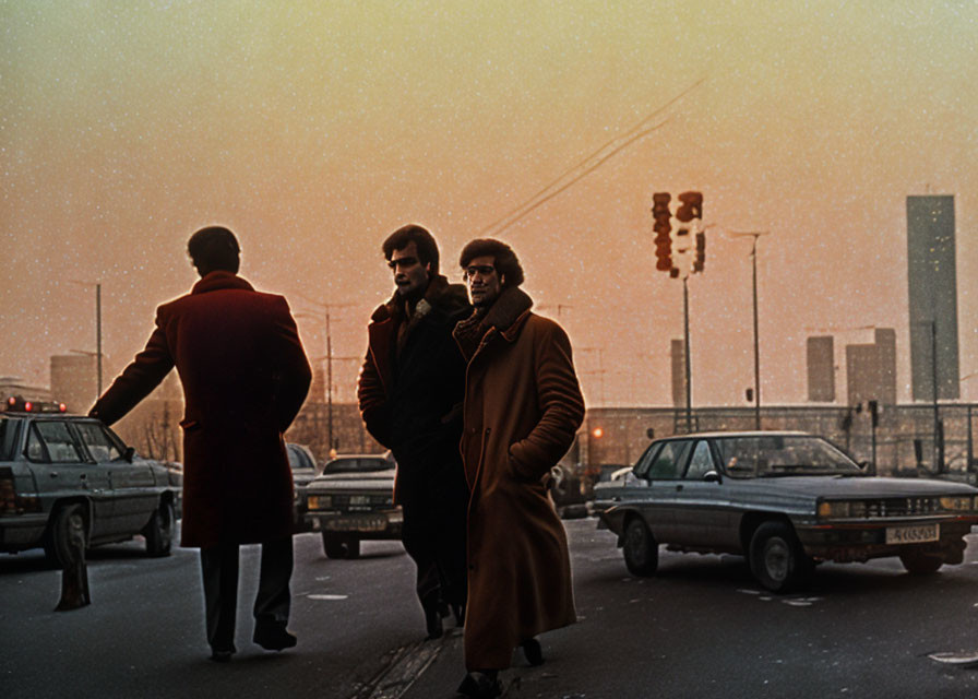 Three men in coats at urban crosswalk with vintage cars and sunset backdrop.