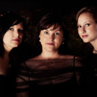 Three Women in Vintage-Inspired Attire on Dark Patterned Background