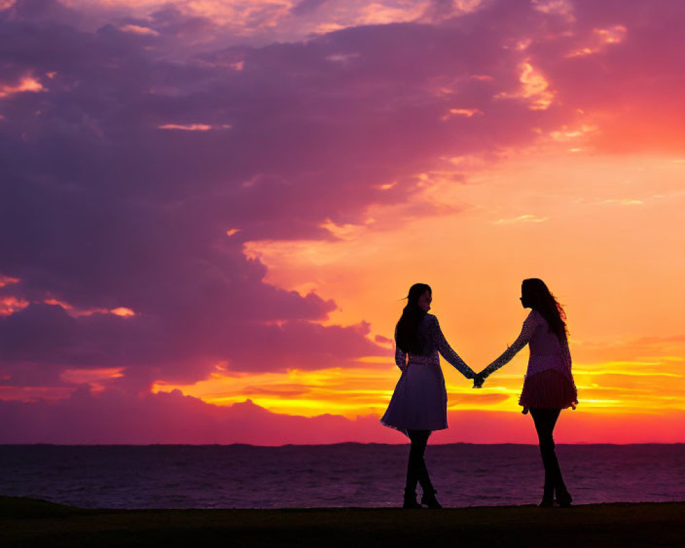 Silhouetted individuals holding hands at vibrant sunset over calm sea