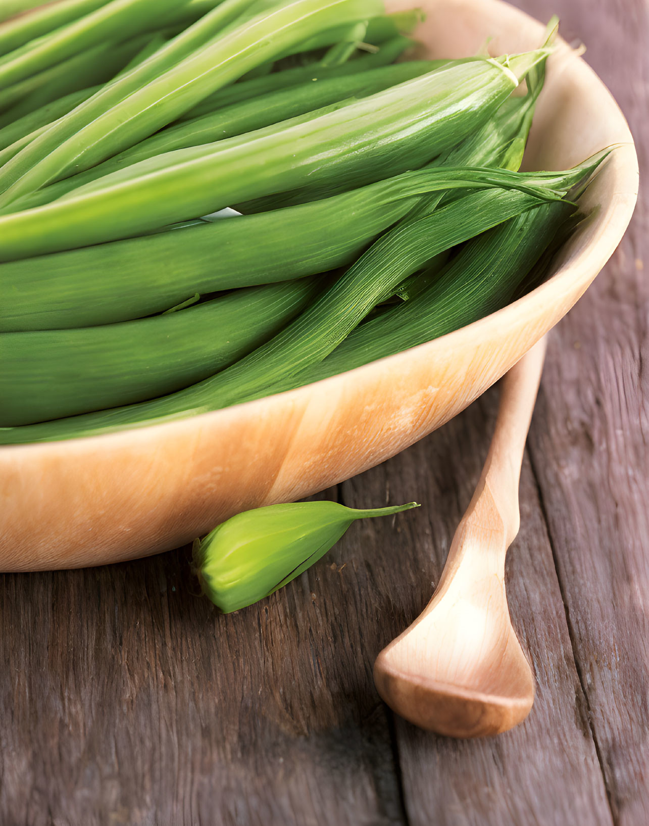 Green leeks in wooden bowl with spoon on rustic table