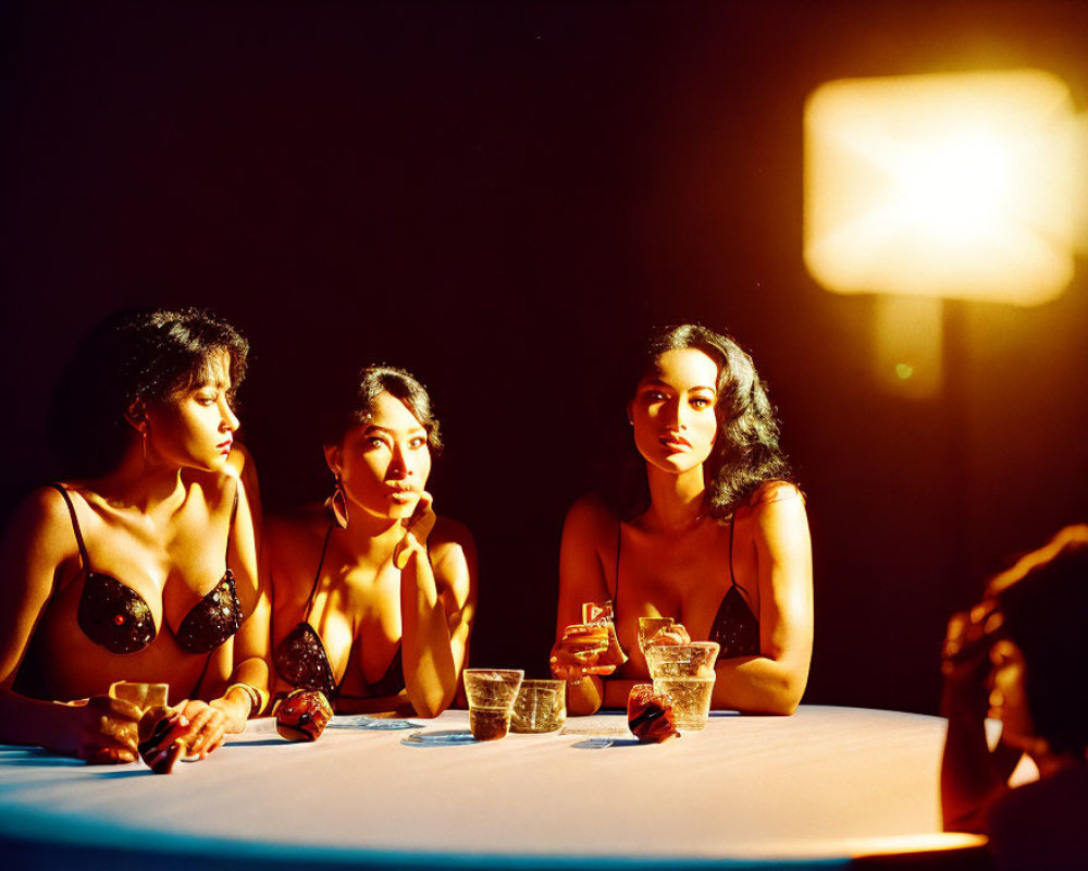 Three Women Sitting at Table Under Warm Light with Drinks