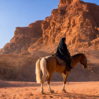 Person in traditional attire riding horse in vast desert with towering rock formations