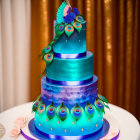 Vibrant blue and purple peacock-themed multi-tiered cake with edible feathers