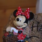 Anthropomorphic female mouse in red polka dot dress peeking from wicker basket surrounded by flowers