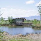 Tranquil landscape with wooden house by lake, lush greenery, mountains, and clear sky