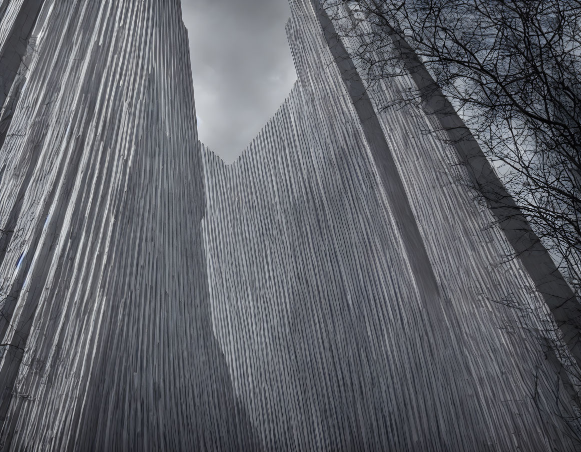 Modern skyscraper with vertical lines design against cloudy sky and bare tree branches.