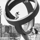 Skateboarder mid-air trick on curved metal sculpture in urban setting