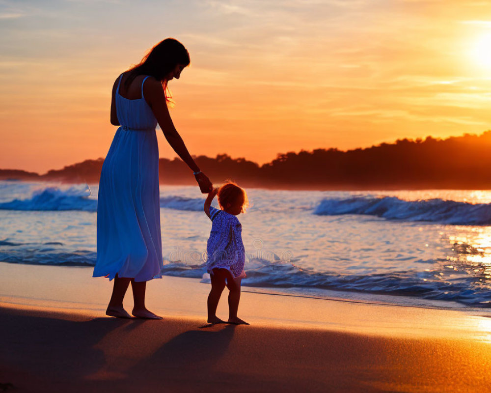 Woman and toddler holding hands on beach at sunset with waves.