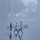 Surfers with boards walking in shallow water under misty sky