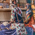 Four women in ornate dresses with floral headdresses amid colorful drapery.