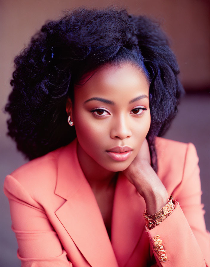 Styled black hair woman in coral blazer poses elegantly.