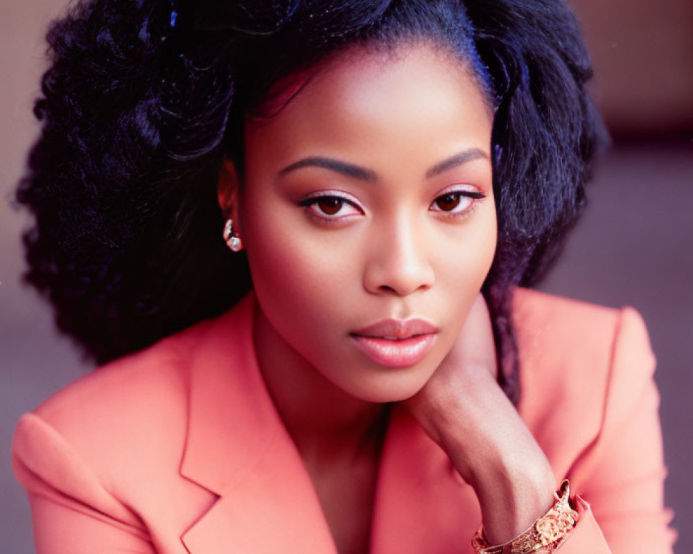 Styled black hair woman in coral blazer poses elegantly.