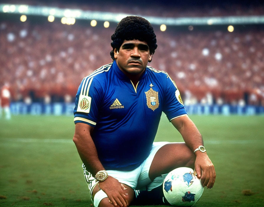 Male soccer player in blue and gold jersey kneeling with ball on pitch.