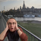 Man sitting by river with hands covering ears in front of town landscape